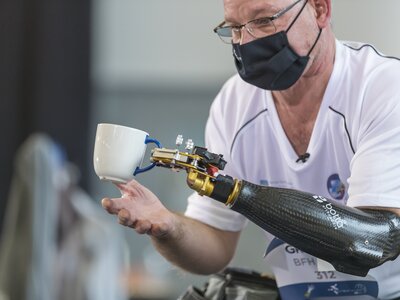 CYBATHLON Pilot hebt eine Teetasse nach oben mithilfe einer Armprothese